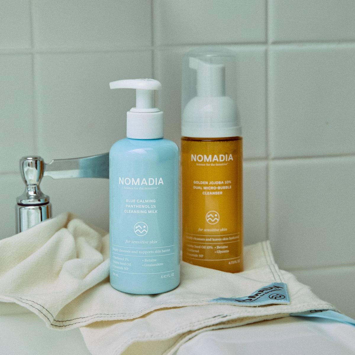 Blue Calming Cleansing Milk and Golden Jojoba Micro-bubble Cleanser on a towel beside a sink