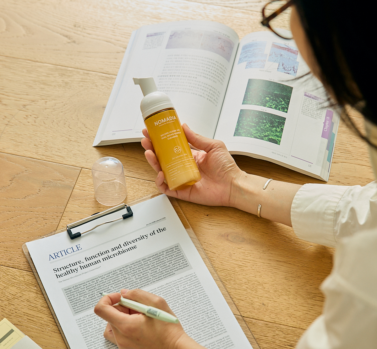Person holding Golden Jojoba Micro-bubble Cleanser while reading and taking notes at a desk