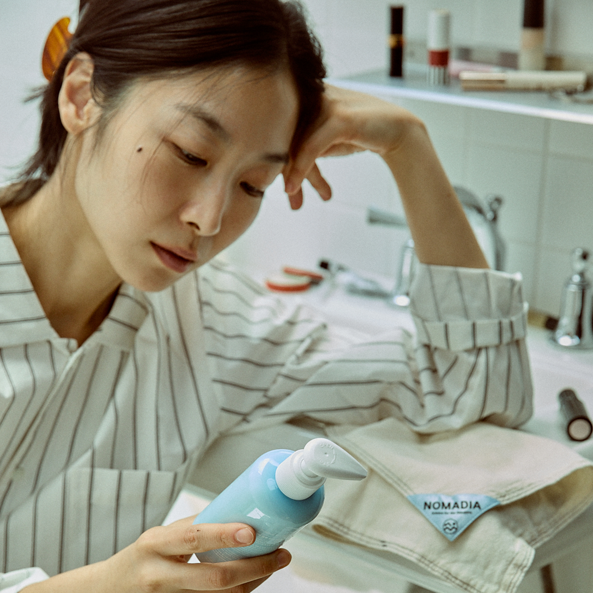 Mujer sosteniendo un frasco de Blue Calming Cleansing Milk junto al lavabo